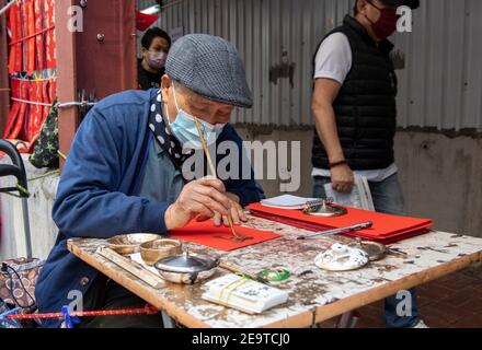 Hongkong, China. Februar 2021, 06th. HONGKONG, HONGKONG SAR, CHINA: FEBRUAR 6TH 2021. Eine Kalligraphie sifu (Meister) arbeitet an der Seite einer belebten Straße in Causeway Bay Hongkong und produziert handbemalte kantonesische Couplets, die für das chinesische Neujahr bereit sind. Mondneujahrescouplets oder Cheun lyun, werden als Dekoration verwendet und haben unterschiedliche glückverheißende Nachrichten, die auf ihnen geschrieben werden. CNY wird am Freitag, 12th. Februar 2021 mit dem Feiertag beginnen, der das Tierkreisjahr des Ochsen ankündigt. Alamy Live Nachrichten/Jayne Russell Kredit: Jayne Russell/Alamy Live Nachrichten Stockfoto