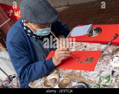 Hongkong, China. Februar 2021, 06th. HONGKONG, HONGKONG SAR, CHINA: FEBRUAR 6TH 2021. Eine Kalligraphie sifu (Meister) arbeitet an der Seite einer belebten Straße in Causeway Bay Hongkong und produziert handbemalte kantonesische Couplets, die für das chinesische Neujahr bereit sind. Mondneujahrescouplets oder Cheun lyun, werden als Dekoration verwendet und haben unterschiedliche glückverheißende Nachrichten, die auf ihnen geschrieben werden. CNY wird am Freitag, 12th. Februar 2021 mit dem Feiertag beginnen, der das Tierkreisjahr des Ochsen ankündigt. Alamy Live Nachrichten/Jayne Russell Kredit: Jayne Russell/Alamy Live Nachrichten Stockfoto