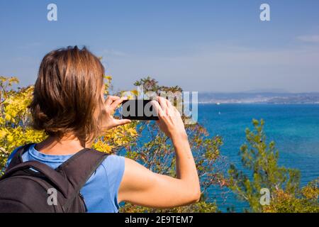 Eine Wanderin mit einem Backpacker, der mit ihrem Smartphone ein Foto vom Meer gemacht hat. Strunjan, Slowenien Stockfoto