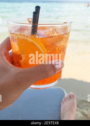 Hand hält ein Glas aperol Spritz Cocktail im Sommer Gegen das Meer Stockfoto