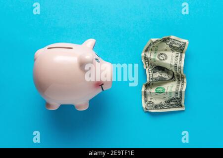 Sparschwein mit einer zerknitterten Dollar-Bancnote auf blauem Hintergrund. Minimaler Coronavirus-Ausbruch. Sparkonzept. Stockfoto