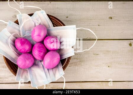 Ostern traditionelle rosa gefärbte Eier mit Schutzmasken in einem Weidenkorb als Konzept für die COVID-19 oder Coronavirus Pandemie. Impfung und imm Stockfoto