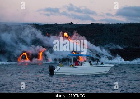 Ein Boot bekommt einen genaueren Blick auf die Pahoehoe Lava, die von Kilauea in den Pazifischen Ozean bei Sonnenaufgang in der Nähe von Kalapana, Big Island, Hawaii fließt. Stockfoto