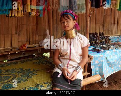 Ein kleines Mädchen aus dem Stamm der Karen mit einer einzigartigen Halskette um ihren langen Hals, sitzt zurückgelehnt und wartet auf Käufer von Handwerksprodukten Stockfoto
