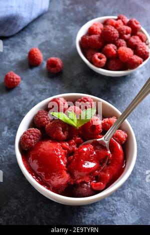 Himbeer-Sorbet, Eisportionierer mit frischen Beeren in Schüssel auf blauem Stein Hintergrund. Leckeres sommerliches kaltes Dessert. Nahaufnahme Stockfoto
