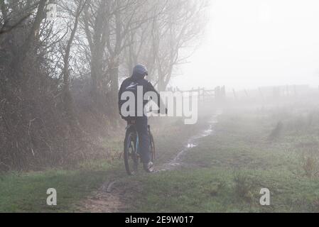 Avon Valley Footpath, Burgate, Fordingbridge, New Forest, Hampshire, UK, 6th February, 2021, Wetter: Nebel und Nebel umhüllen die Landschaft und die Temperaturen sind nahe an eiskalten frühen Morgen vor einer Zeit von sehr kaltem Wetter. Ein Radfahrer macht seinen Weg durch die Murche. Kredit: Paul Biggins/Alamy Live Nachrichten Stockfoto