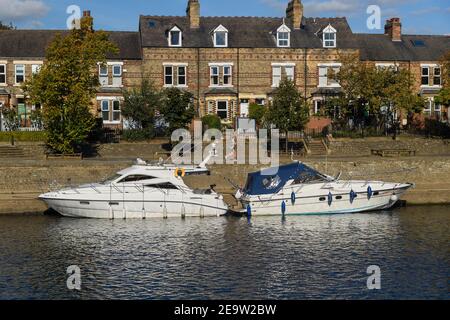 River Ouse in York - Boote (Freizeit-Cruiser) am Kai durch Reihe von Häusern (Terrasse) und Jogger auf Flussweg - North Yorkshire, England, Großbritannien. Stockfoto