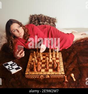 Frau spielt Schach mit einem Computerprogramm am Telefon. Schachspiel zu Hause mit künstlicher Intelligenz, KI auf dem Handy Stockfoto