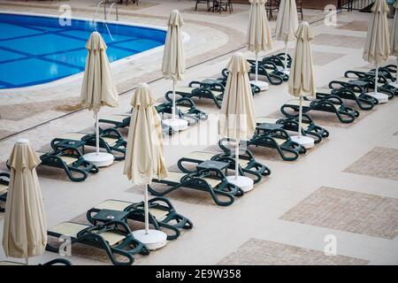 Plastikliegen und Sonnenschirme für den Sonnenschutz sind platziert Auf den Fliesen am Pool im Erholungsgebiet Stockfoto