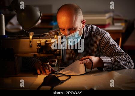 Mann arbeitet mit Nähmaschine tun hausgemachte Gesichtsmaske für Verhindern und verhindern der Verbreitung von Corona-Viren Stockfoto