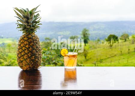 Ein Glas Michelada mit Eis und Limette auf einer Bar mit Ananas und Dschungel im Hintergrund. Stockfoto