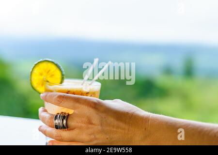 Hand hält ein Glas Michelada mit Eis und Zitrone mit dem Dschungel im Hintergrund aus Fokus. Costa Rica Stockfoto