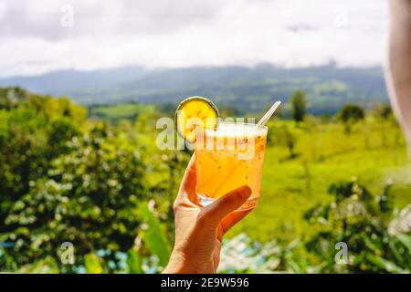 Eine Frau, die ein Glas Michelada vor einer Waldlandschaft hält. Costa Rica Gastronomie Stockfoto