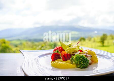 Teller gegrilltes Fischfilet mit Gemüse auf einem Holztisch vor dem Wald. Costa Rica Gastronomie Stockfoto
