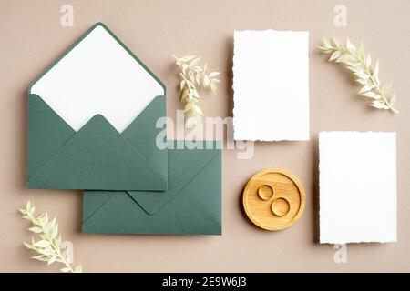 Feminine Hochzeitsbriefpapier-Set. Leere Grußkarte, grüne Umschläge, getrocknete Blumen, goldene Ringe auf pastellbeigem Hintergrund. Rustikale Hochzeit invitati Stockfoto