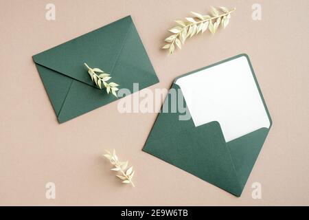 Grüne Umschläge und getrocknete Blumen auf pastellbeigem Hintergrund. Hochzeitseinladung Mockup, elegante rustikale Grußkarte. Stockfoto