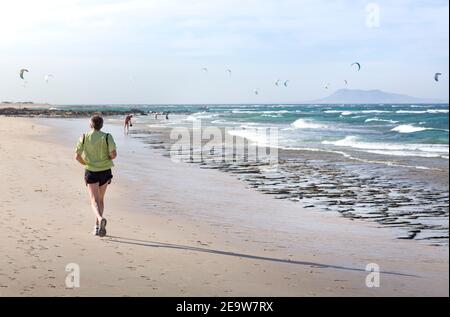 FUERTEVENTURA, SPANIEN - 10. Mai 2013. Reifer Mann beim Joggen am Strand mit Kitesurfern im Hintergrund. Corralejo, Fuerteventura, Kanarische Inseln Stockfoto