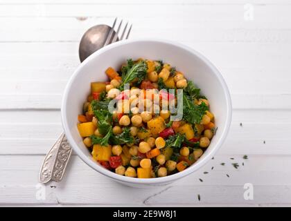 Hausgemachtes Ragout mit Kürbis, Karotten, Paprika, Tomaten, Kichererbsen, Grünkohl und Thymian in einer weißen Schüssel auf weißem Hintergrund. Lecker gesundes Foo Stockfoto
