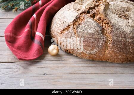 Weihnachtsbacken. Vollkornbrot Roggen Weizenbrot Ofen in Keramikpfanne gebacken. Kein handgefertigtes Brot auf Schneidebrett auf Holz mit festlichem dunkelrotem Handtuch XM kneten Stockfoto