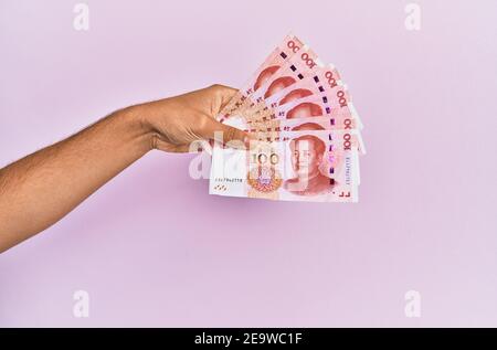 Hispanische Hand mit 100 chinesischen Yuan-Banknoten auf isoliertem rosa Hintergrund. Stockfoto