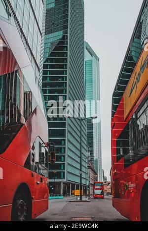London UK Januar 2021 Vertikale Aufnahme eines zwei modernen roten Doppeldeckerbusses, der im absperrten, riesigen Wolkenkratzer auf den leeren Straßen Londons fährt Stockfoto