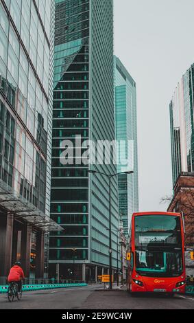 London UK Januar 2021 Vertikale Aufnahme eines modernen roten Doppeldeckerbusses, der in abgesperrten, riesigen Wolkenkratzern auf den leeren Straßen Londons fährt Stockfoto