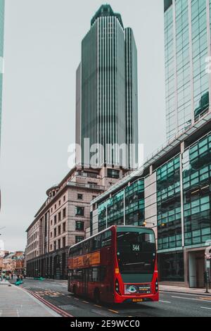 London UK Januar 2021 Vertikale Aufnahme eines modernen roten Doppeldeckerbusses, der in abgesperrten, riesigen Wolkenkratzern auf den leeren Straßen Londons fährt Stockfoto