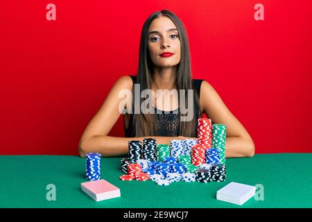 Junge hispanische Frau sitzt auf dem Tisch spielen Poker mit ernster Ausdruck auf Gesicht. Einfach und natürlich Blick auf die Kamera. Stockfoto