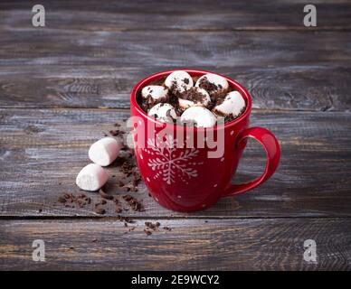 Heiße Schokolade mit Marshmallows und geriebener Schokolade in einem roten Becher auf einem Holztisch, rustikaler Stil. Köstliches weihnachtsgetränk Stockfoto