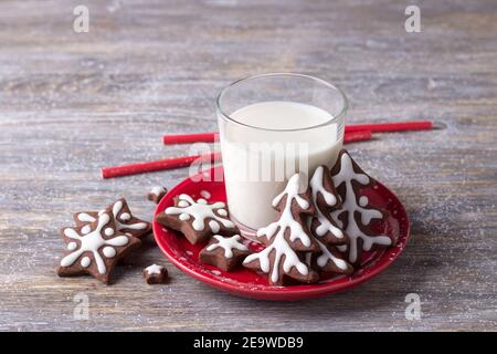 Hausgemachte Weihnachts-Schokoladenkekse, dekoriert mit Glasur, mit einem Glas Milch auf einem Holztisch. Selektiver Fokus. Horizontal Stockfoto