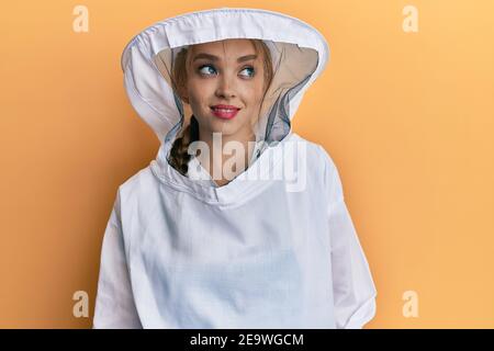 Schöne blonde kaukasische Frau trägt schützende Imker Uniform lächelnd Blick zur Seite und starrte weg denken. Stockfoto