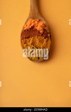 Holzlöffel mit Cayennearten Curcuma Curry und würzig auf ockerem Hintergrund..orange Farbe Lebensmittel. Flach legen Holzlöffel mit Arten. Pulverförmige Saison Stockfoto