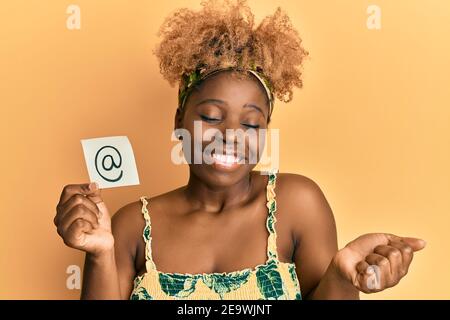 Junge afrikanische Frau mit afro Haar hält Online-Mail-Symbol auf Papier schreien stolz, feiert Sieg und Erfolg sehr aufgeregt mit erhobenem Arm Stockfoto