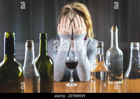 Alkoholismus Konzept mit Frau und Flaschen im Innenbereich. Echte Menschen mit Alkoholmissbrauch Problem. Selektiver Fokus auf Flaschen Stockfoto