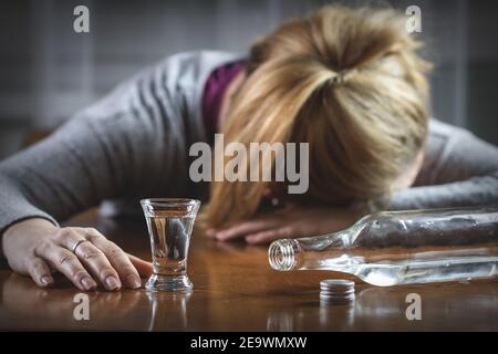 Betrunkene Frau schläft auf dem Tisch nach dem Trinken von Wodka. Alkoholmissbrauch Konzept. Harter Schnaps in Schnapsglas und Flasche Stockfoto