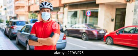 Junge Lieferung Mann trägt Fahrradhelm und Coronavirus Schutz medizinische Maske an der Straße der Stadt stehen. Stockfoto