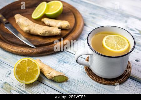 Ingwerwurzel und heißer Tee mit Zitronenscheibe in weißem Becher. Gesundes Lifestyle-Konzept. Heißes Getränk in der Teetasse auf dem Holztisch Stockfoto