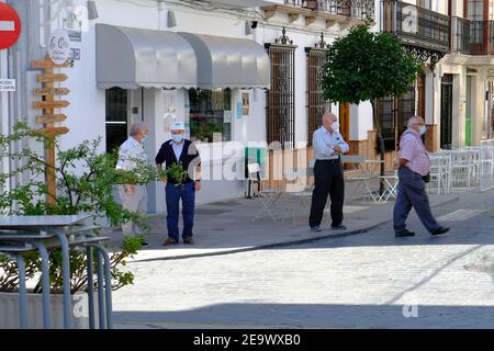 Ältere männliche Bewohner auf dem Dorfplatz, mit Masken und Distanzierung während der Covid-Pandemie im Sommer 2020. Carcabuey, Andalusien, Spanien Stockfoto