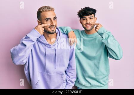 Homosexuell Homosexuell Paar zusammen stehend tragen lässige Kleidung zeigt mit der Hand Finger auf Gesicht und Nase, lächelnd fröhlich. Beauty-Konzept Stockfoto