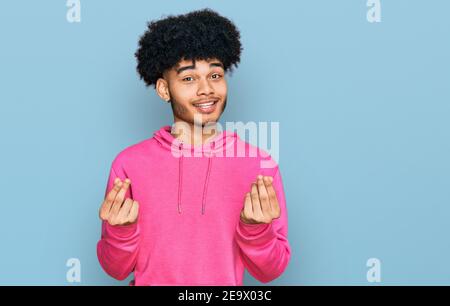 Junger afroamerikanischer Mann mit Afro-Haaren trägt beiläufiges rosa Sweatshirt tun Geld Geste mit den Händen, um Gehaltszahlung fragen, Millionär Busine Stockfoto
