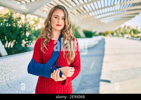 Junge blonde Mädchen mit ernsten Ausdruck verletzt mit Arm Sling stehen im Park. Stockfoto