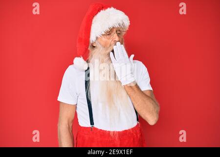 Alter älterer Mann mit grauen Haaren und langem Bart trägt weißes T-Shirt und weihnachtsmann Kostüm gelangweilt gähnend müde Abdeckung Mund mit der Hand. Rastlos und Stockfoto
