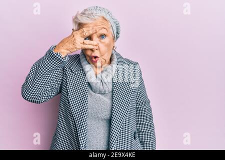 Ältere grauhaarige Frau trägt Wolle Winter Pullover Blick in Schock über Gesicht und Augen mit der Hand, Blick durch die Finger Angst Stockfoto
