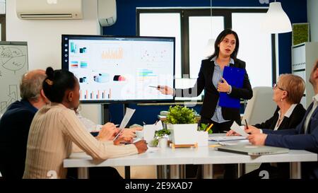 Weibliche Projektmanagerin, die ein Finanzmeeting mit statistischen Grafiken und Diagrammen auf einem interaktiven Whiteboard-Touchscreen-Gerät abhält. Executive Director arbeitet im Broadroom der Kreativagentur. Stockfoto