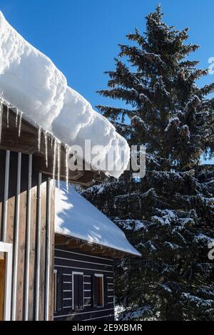 Schneebedeckte Berghütte mit Eiszapfen am sonnigen Wintertag Stockfoto