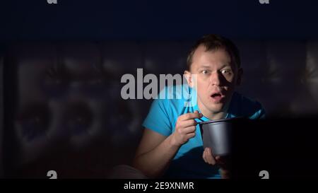 Ein Mann schaut nachts Fernsehen und isst Eis. Überraschendes Gesicht. Bewegte Kamera Stockfoto