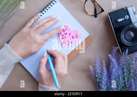 Holzherz LIEBE und Frau Hände hinter Notebook auf dem Tisch und Retro-Kamera. Konzept für das Schreiben von Briefen. Symbol für Herzform. Valentinstag - romantisch Stockfoto