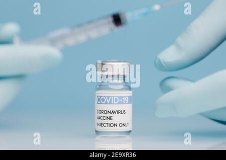 Nahaufnahme der Ernte unkenntlich Arzt in Handschuhen Füllen Spritze mit Impfstoff aus Coronavirus in Glasfläschchen auf blauem Hintergrund Stockfoto