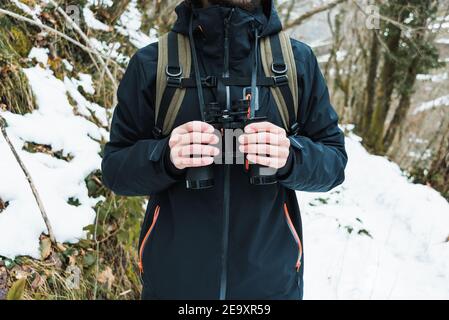 Kurzer unerkennbarer männlicher Wanderer in warmer Kleidung, der im Schnee steht Winterwald mit Fernglas Stockfoto