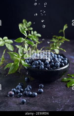 Von oben der Schüssel mit dem Haufen reif gesund gewaschen Heidelbeeren auf schwarzem Marmortisch mit grünen Blättern in platziert Küche Stockfoto